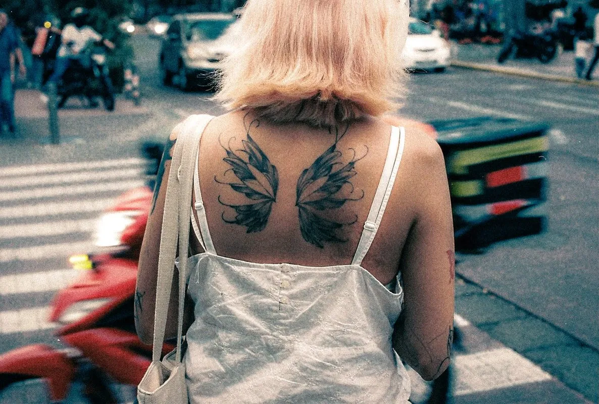 Mujer de espaldas con un tatuaje de alas en un cruce peatonal